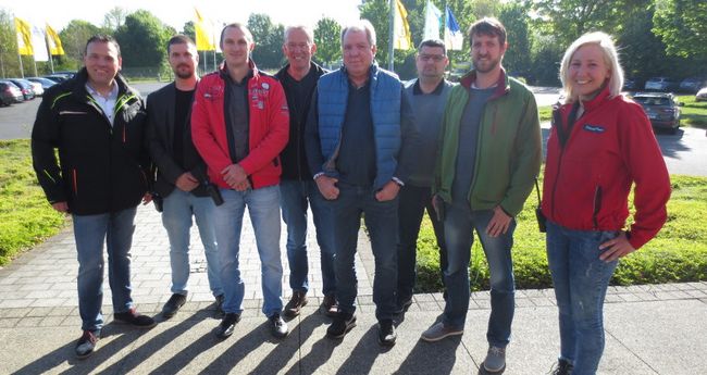 Sieben Kursteilnehmer eines Gruppen-Trainings für Pkw und die Instruktorin haben sich zum Gruppenbild aufgestellt. Alle lächeln in die Kamera. Der Hintergrund ist frühlingshaft.