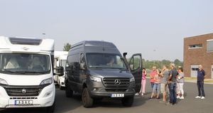 Eine Gruppe Kursteilnehmer steht neben einem schwarzen Transporter auf dessen Fahrersitz eine Kursteilnehmerin Platz genommen hat. Sie schaut durch die geöffnete Fahrertür zur Gruppe. Im Hintergrund ist das Seminargebäude zu sehen.