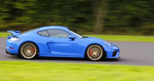 Königsblauer Porsche auf der Kurvenlinie, trockener Asphalt und frisches grünes Gras entlang der Strecke. Die Themen „Kurve – Kurvenlinie und Grenzbereich” sind fester Bestandteil unserer sportiven Trainingsangebote.