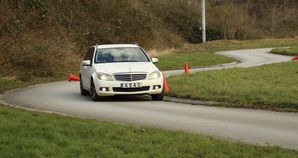 Pkw BGHM-Training – Ein weißer Mercedes Kombi ist auf kurvenreicher Strecke zu sehen, er passiert einige Pylonen.