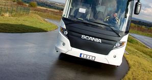 In Nahaufnahme sieht man den Busfahrer in schwarz-gelber Jacke im weißen Scania-Bus mit schwarzer Front bei einer Fahrt auf kurvenreicher Strecke.